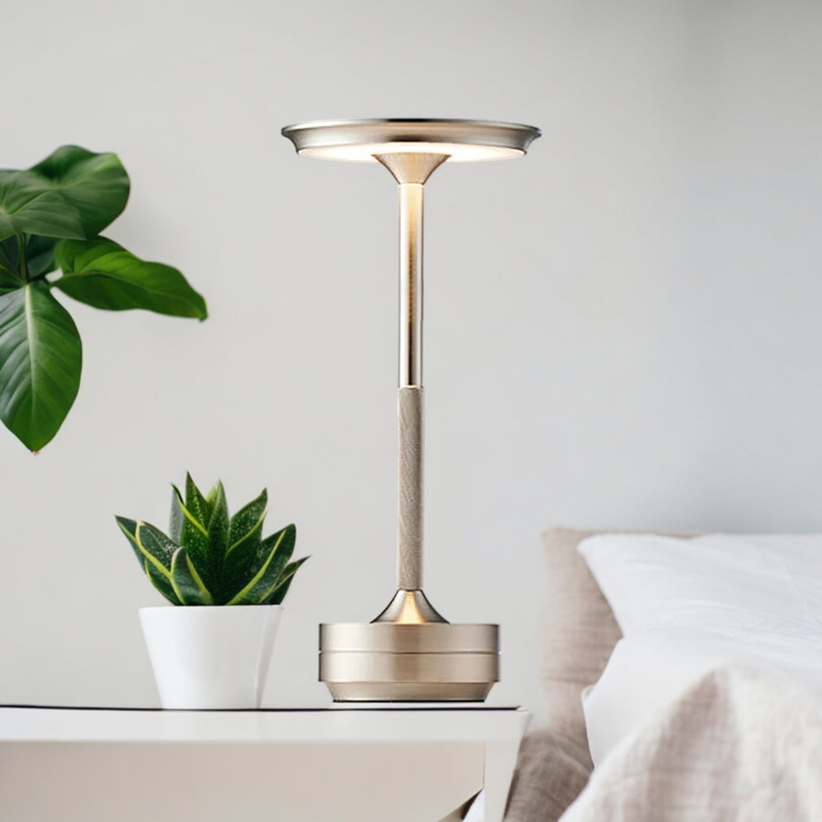 Silver Aura lamp lit on a white bedside table